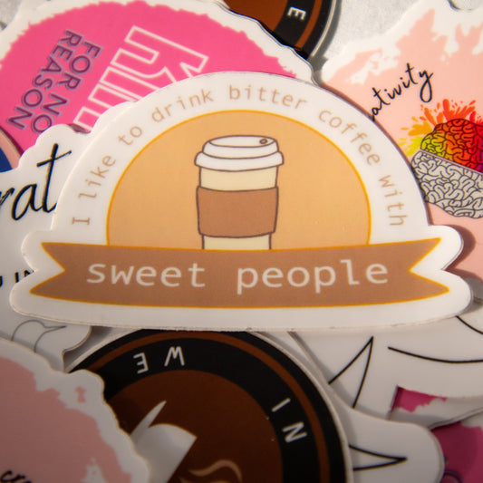 Aesthetic coffee sticker in a pile of colorful vinyl decals, featuring the phrase “I like to drink bitter coffee with sweet people”