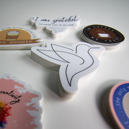 Stack of waterproof bird stickers for water bottles, featuring the Poetry Rise dove logo with other affirmation and coffee-themed designs