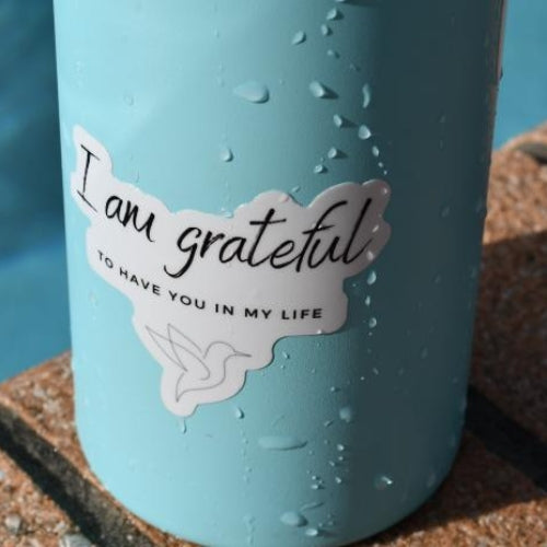 Gratitude sticker on a blue water bottle, reads 'I am grateful to have you in my life' in black script